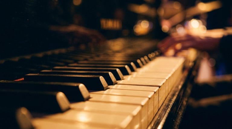 Close-up of piano keys with warm stage lighting and blurred jazz musicians performing in background