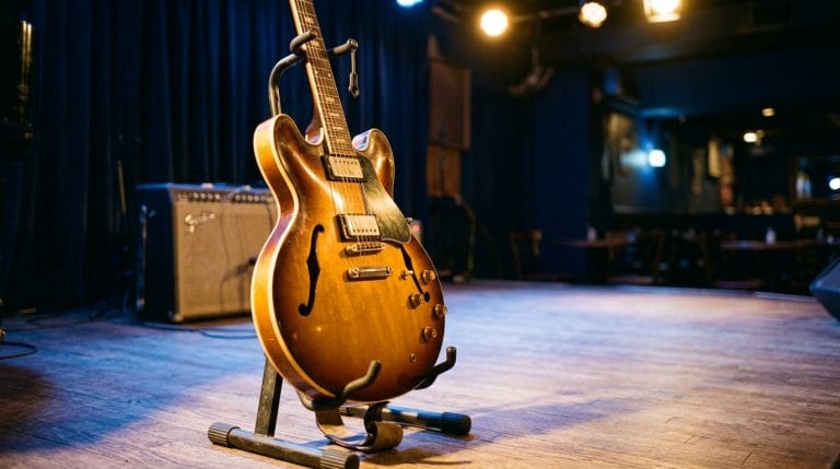 Semi-hollow body electric guitar on stage with amplifier and blue curtain backdrop